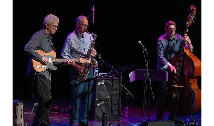 jazz trio of men including guitarist, sax player, and stand up bassist on stage playing